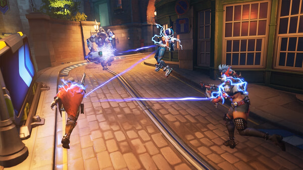 Overwatch® screenshot: Characters engage in a dynamic street battle, with energy beams connecting opponents in a vibrant urban setting.